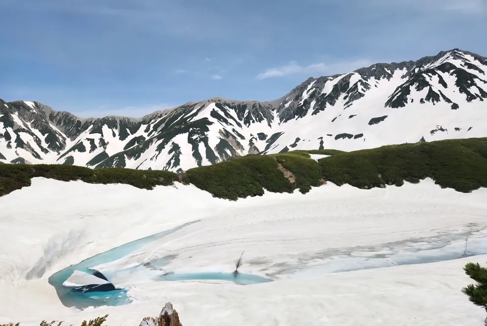 雪に覆われたみくりが池と、雪の残る立山の山並み。池の一部だけ青い水面が見えている