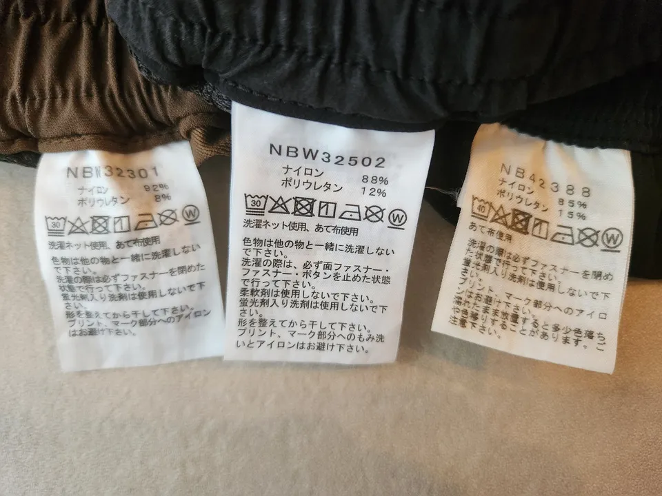 3本の品質表示タグを並べた写真。左からアルパインライトNBW32301（ナイロン92%・ポリウレタン8%）、バーブライトスリムNBW32502（ナイロン88%・ポリウレタン12%）、フレキシブルアンクルNB42388（ナイロン85%・ポリウレタン15%）