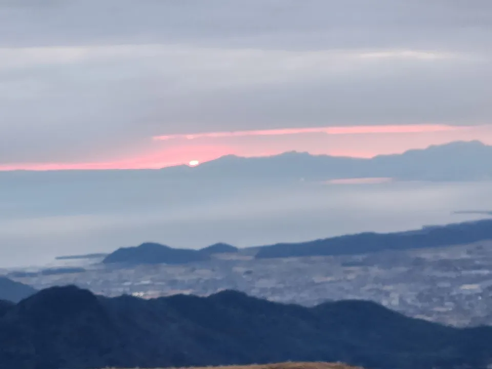 冬の平尾台から見た朝焼け。山並みの向こうの雲の切れ間に日が出て、手前に街と海が広がる
